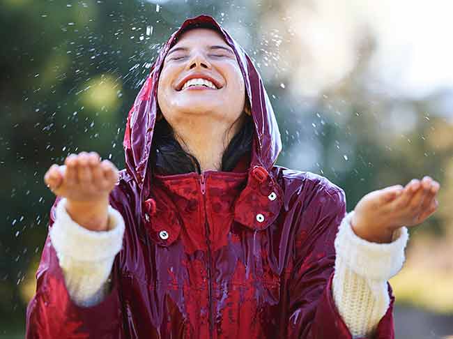A person wearing a red raincoat and white gloves stands smiling in the rain with his eyes closed and arms raised.
