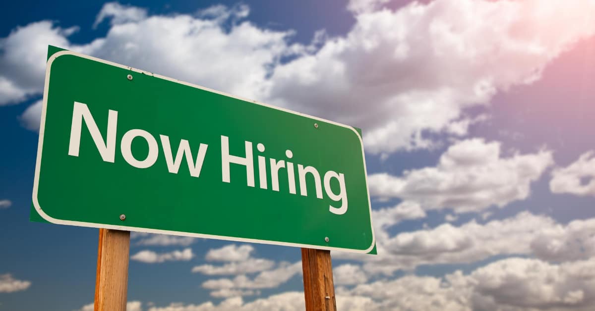 Green Now Hiring sign under Iligan Citys bahagyang maulap na kalangitan na may sikat ng araw na dumadaloy mula sa kanang sulok sa itaas.