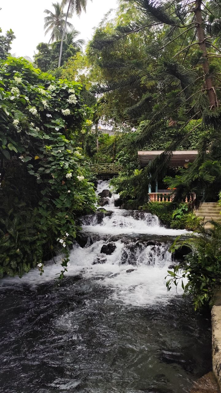 Cascading Iligan City waterfalls na napapaligiran ng mayabong na luntian at maliit na gazebo sa kanan.