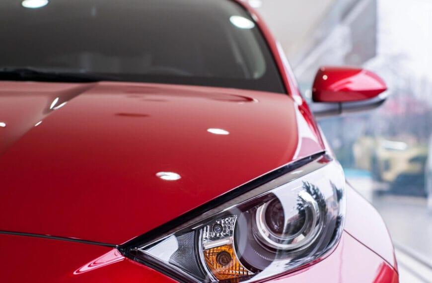 Close-up ng makintab na pulang sulok ng kotse sa harapan, na nakatuon sa headlight at side mirror nito sa isang showroom ng kotse sa Iligan.