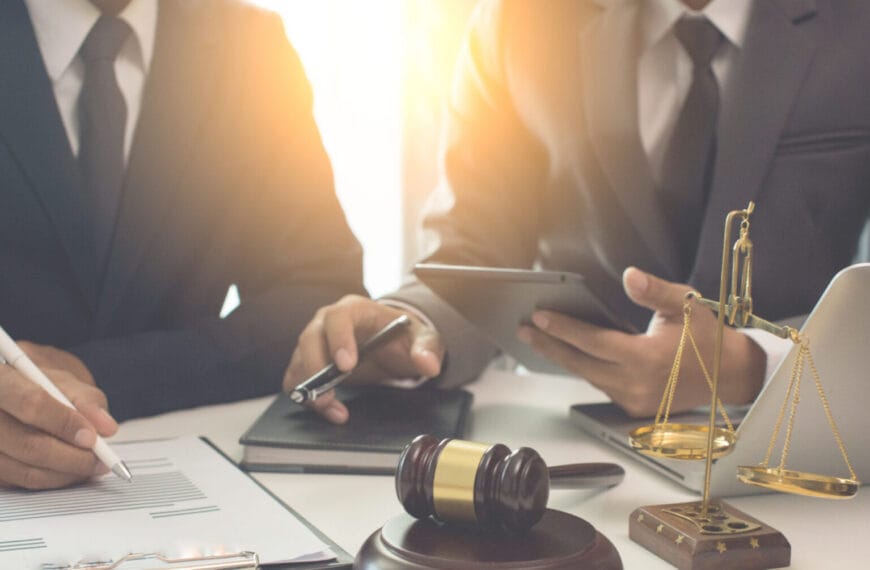 Dalawang tao na nakasuot ng suit, kabilang ang isang abogado ng Iligan, ang nagtatrabaho sa isang desk na may dalang mga legal na dokumento, isang gavel, at isang laptop.