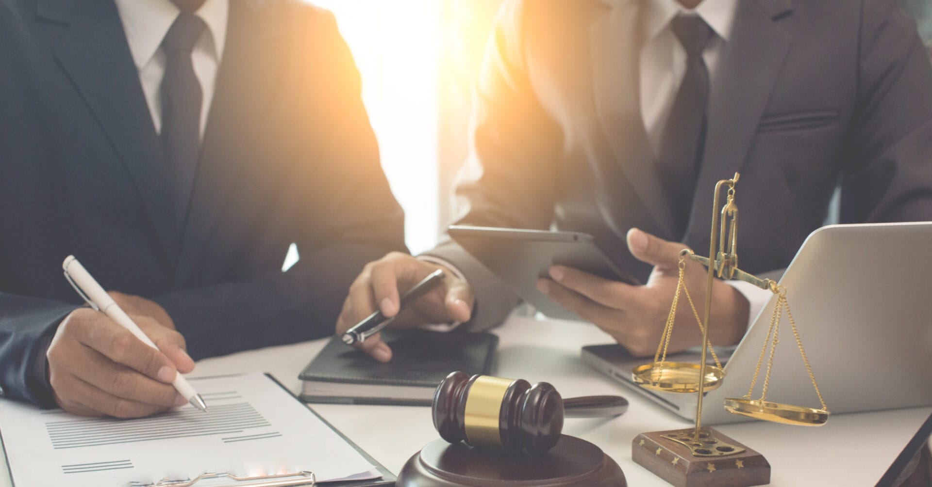 Dalawang tao na nakasuot ng suit, kabilang ang isang abogado ng Iligan, ang nagtatrabaho sa isang desk na may dalang mga legal na dokumento, isang gavel, at isang laptop.