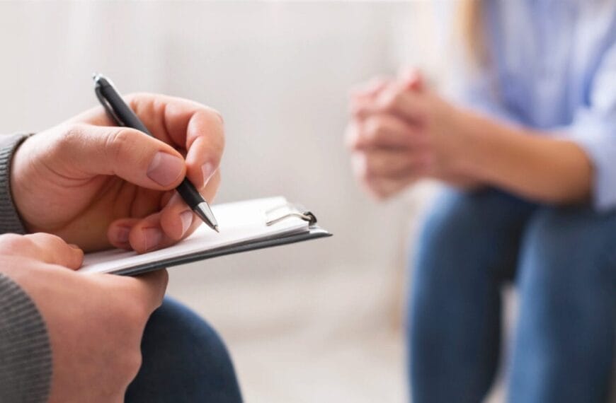 Close up ng isang psychiatrist sa Northern Mindanao na nagsusulat sa clipboard habang ang isang tao ay nakaupo sa tapat at nakahawak ang mga kamay.
