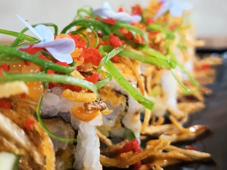 close up ng mga urban cafe signature sushi roll na may isda roe, berdeng sibuyas, at nakakain na bulaklak.