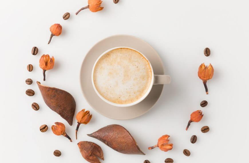 Ang isang tasa ng kape sa isang pinggan ay nakaupo sa gitna ng mga pinatuyong dahon, orange buds, at beans-perpekto para sa mga umaga ng Makati.