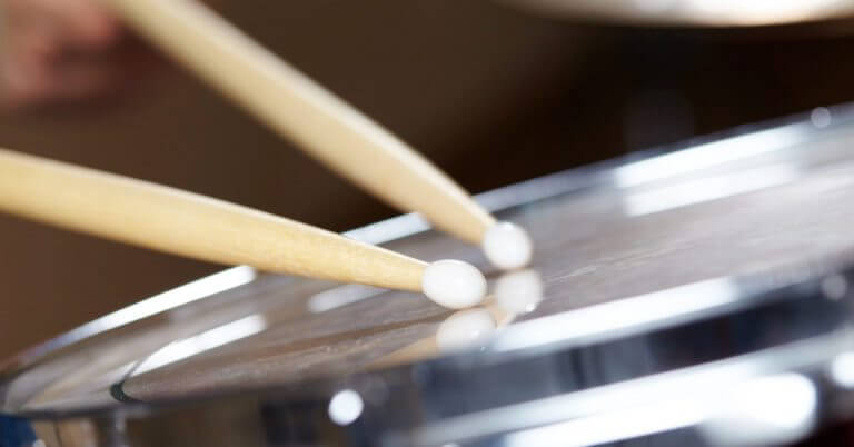 Dalawang kahoy na drumstick na tumatama sa isang makintab na snare drum sa Diyandi Festival Drum and Lire Competition.