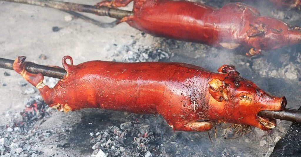 isang buong inihaw na baboy sa isang laway sa ibabaw ng mainit na uling, hinahain na may ginintuang kayumanggi, malutong na balat ng lechon.