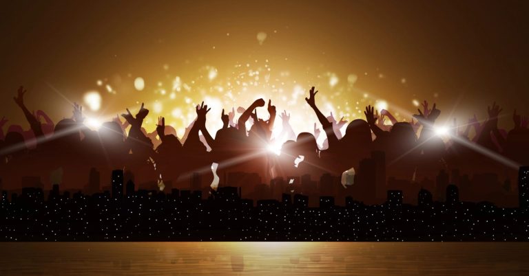 Silhouetted crowd na may nakataas na mga kamay sa isang konsiyerto ng Kasadya, skyline ng lungsod sa ibaba, ginintuang ilaw na nagniningning sa background.