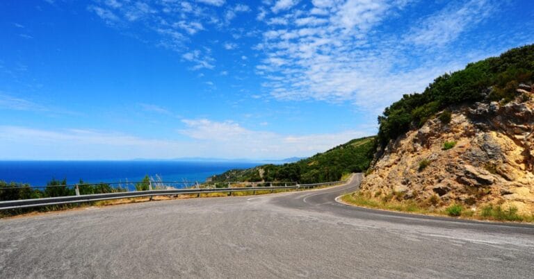 Hubog na kalsada sa baybayin na may guardrail, asul na dagat, at luntian—mainam para sa isang pakikipagsapalaran sa ruta ng paglalakbay sa Mindanao.