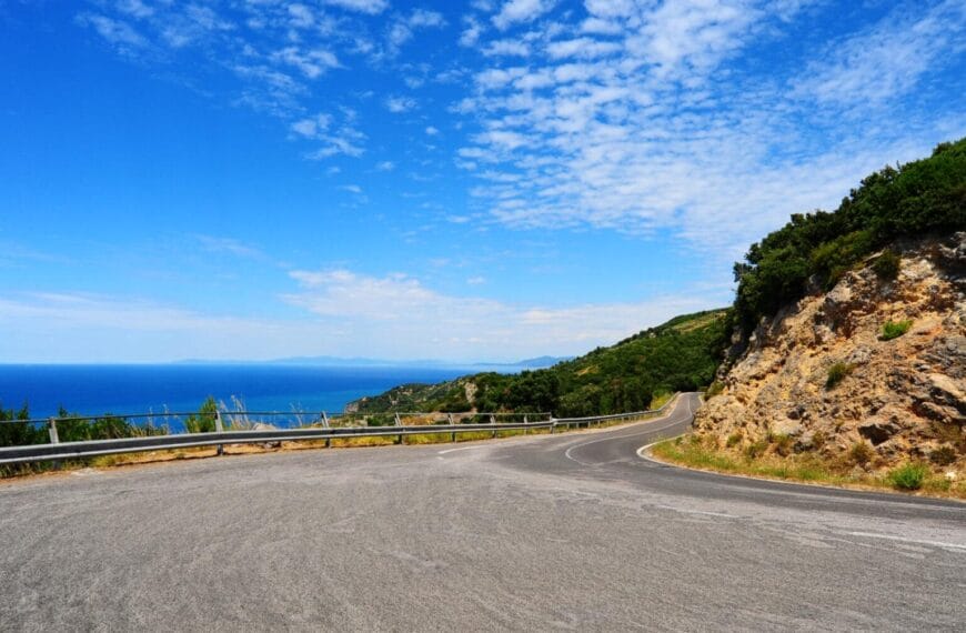 Hubog na kalsada sa baybayin na may guardrail, asul na dagat, at luntian—mainam para sa isang pakikipagsapalaran sa ruta ng paglalakbay sa Mindanao.