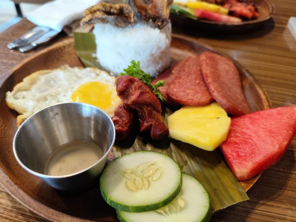 isang kahoy na plato na may kanin, pritong itlog, sausage, at marami pa-perpekto para sa anumang pagkain sa Urban Coffee Studio bukas 24/7.