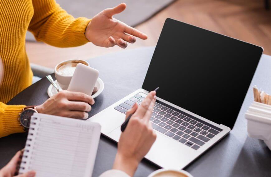 Tinalakay ng dalawang tao ang mga pagkakataon sa freelancing sa isang mesa na may laptop, kape, at telepono sa isang maginhawang setting.