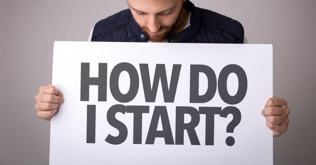 a man holds a “how do i start?” sign, seeking iligan business registration guidance against a plain background.