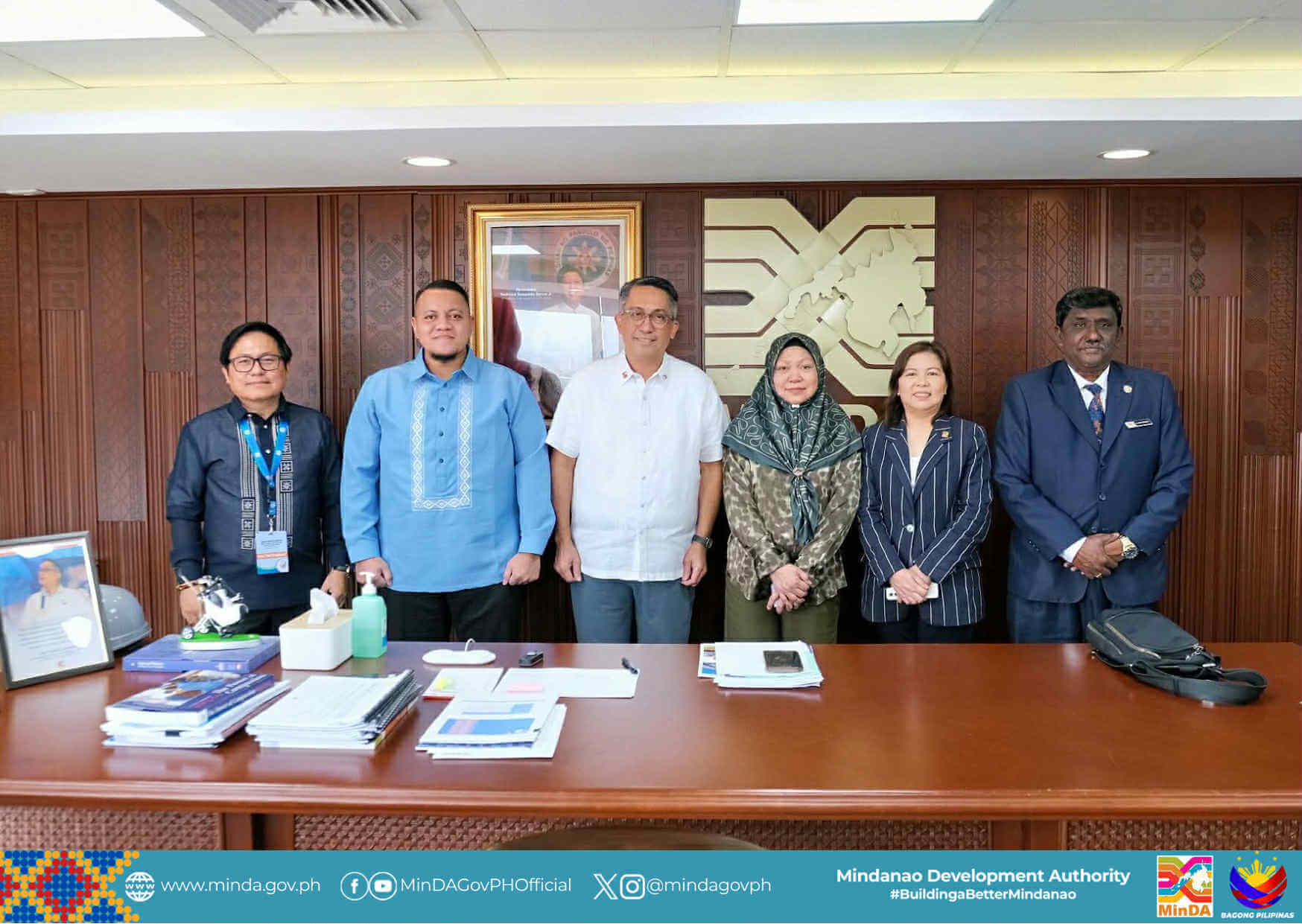 six people stand smiling behind an office desk, celebrating philippines chairmanship of bimp eaga in mindanao.