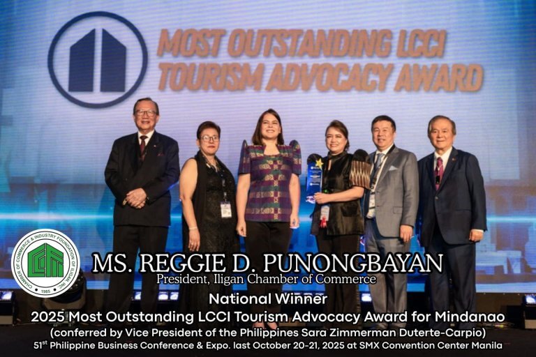 six people stand on stage holding an award, with a blue backdrop and text about a tourism advocacy award.