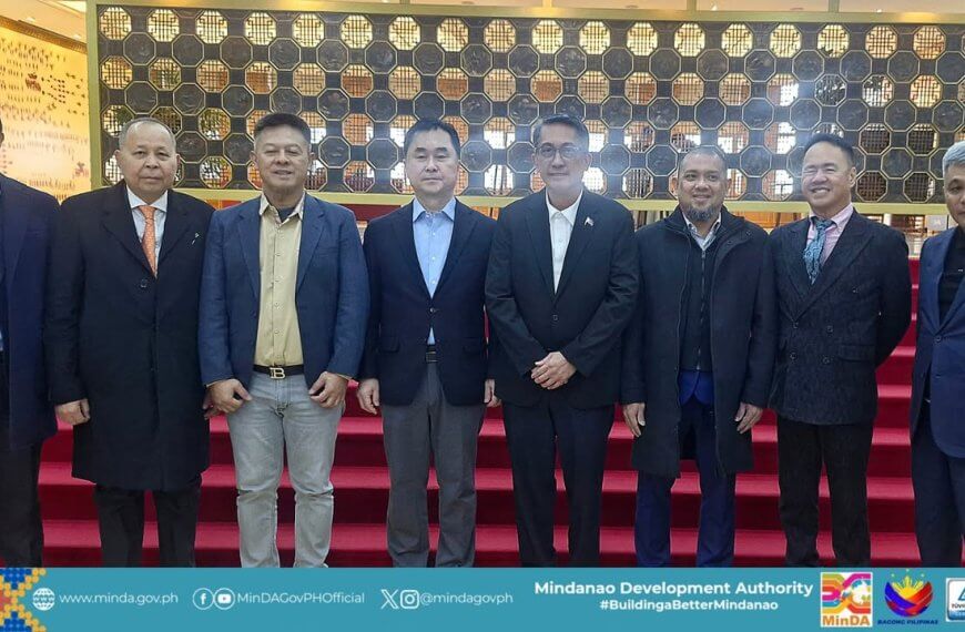 eight men in suits stand in a row on red carpeted stairs in front of a decorative wooden wall.