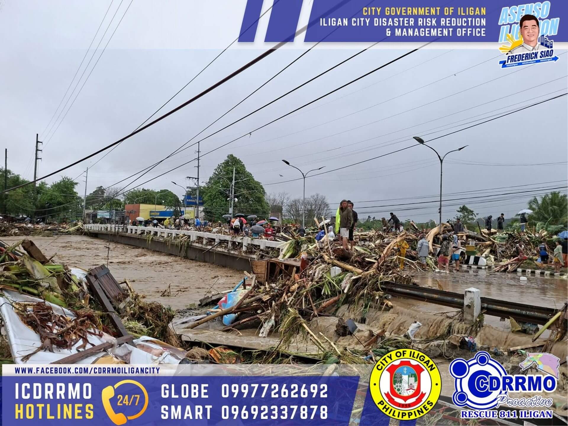 flooded road in iligan city covered with debris and damaged trees, with cloudy skies and emergency hotlines displayed.