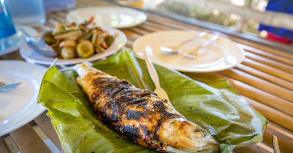 grilled whole fish on a banana leaf, a must visit spot in any mindanao travel guide, served on a bamboo table.