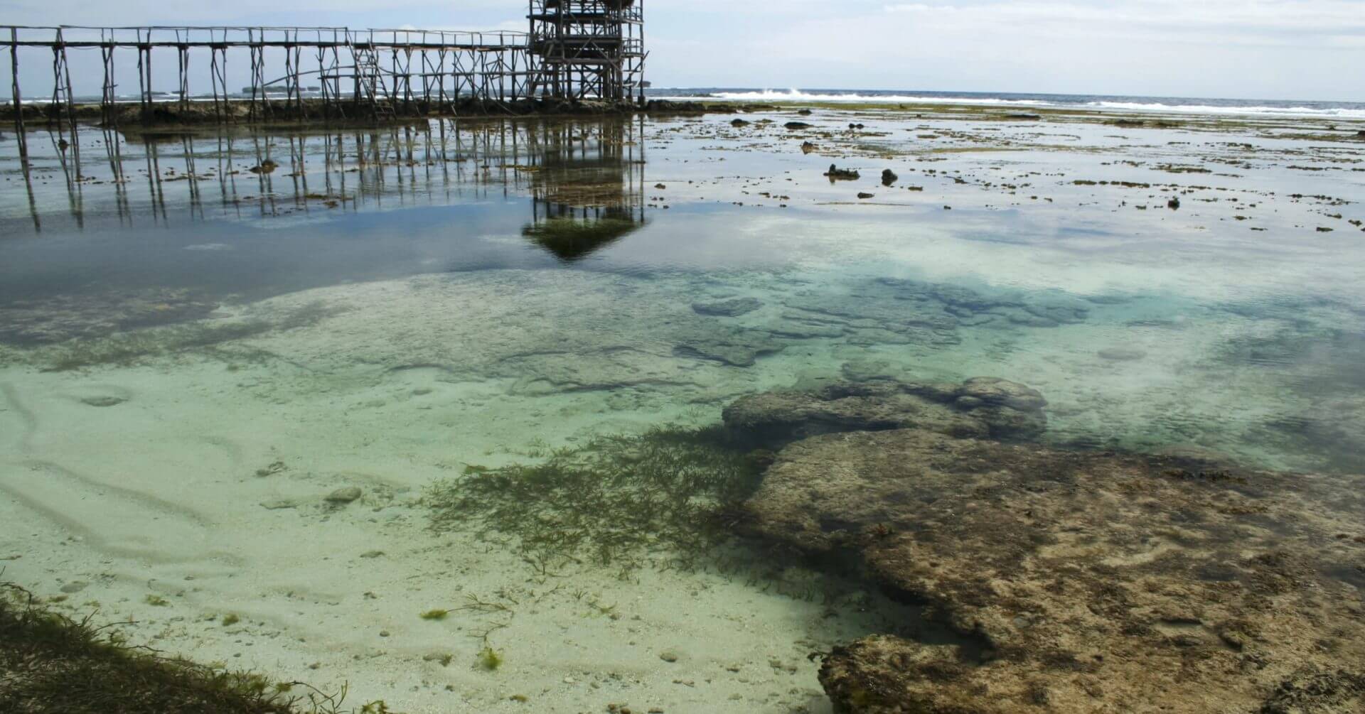 clear shallow tide pool with rocks and seaweed—one of mindanao travel guide’s must visit spots; pier in background.