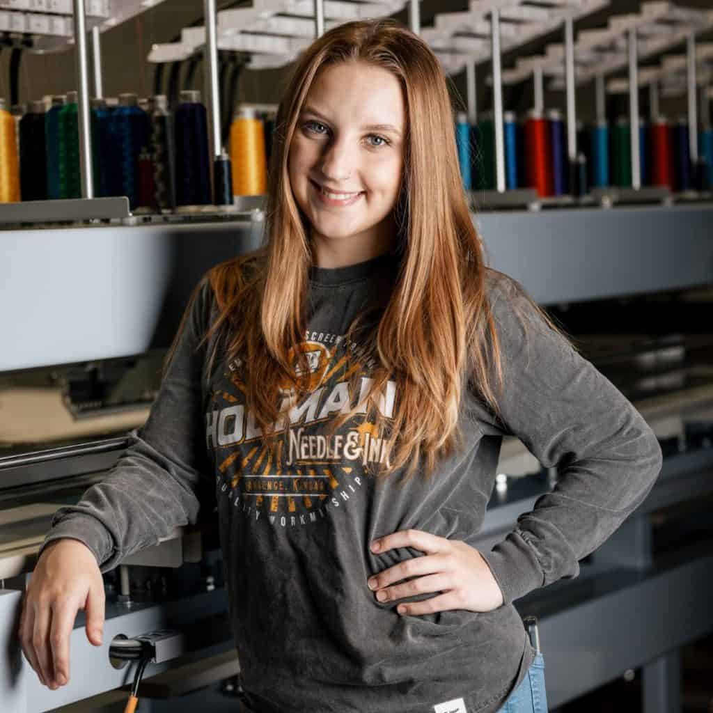 El líder de operaciones, Sidney Budinas, de pie junto a una máquina de bordar personalizada