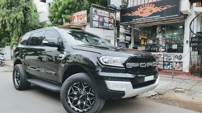 Black Ford SUV parked in front of a car accessories customization shop with various signs and trees in the background.