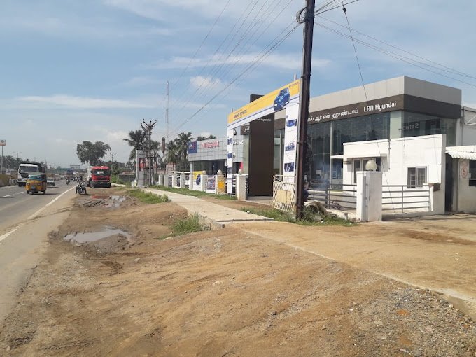 Roadside car showroom with a Hyundai sign, trucks passing by, and a clear sky in the background.