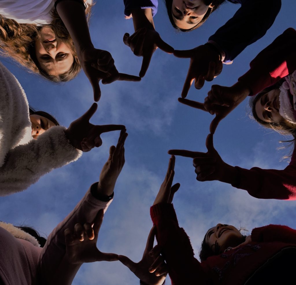 Instituto Internacional de Teología a Distancia – Un grupo de personas en círculo, vistas desde abajo contra el cielo azul, une las manos formando estrellas, símbolo de misión compartida. – formación teológica online