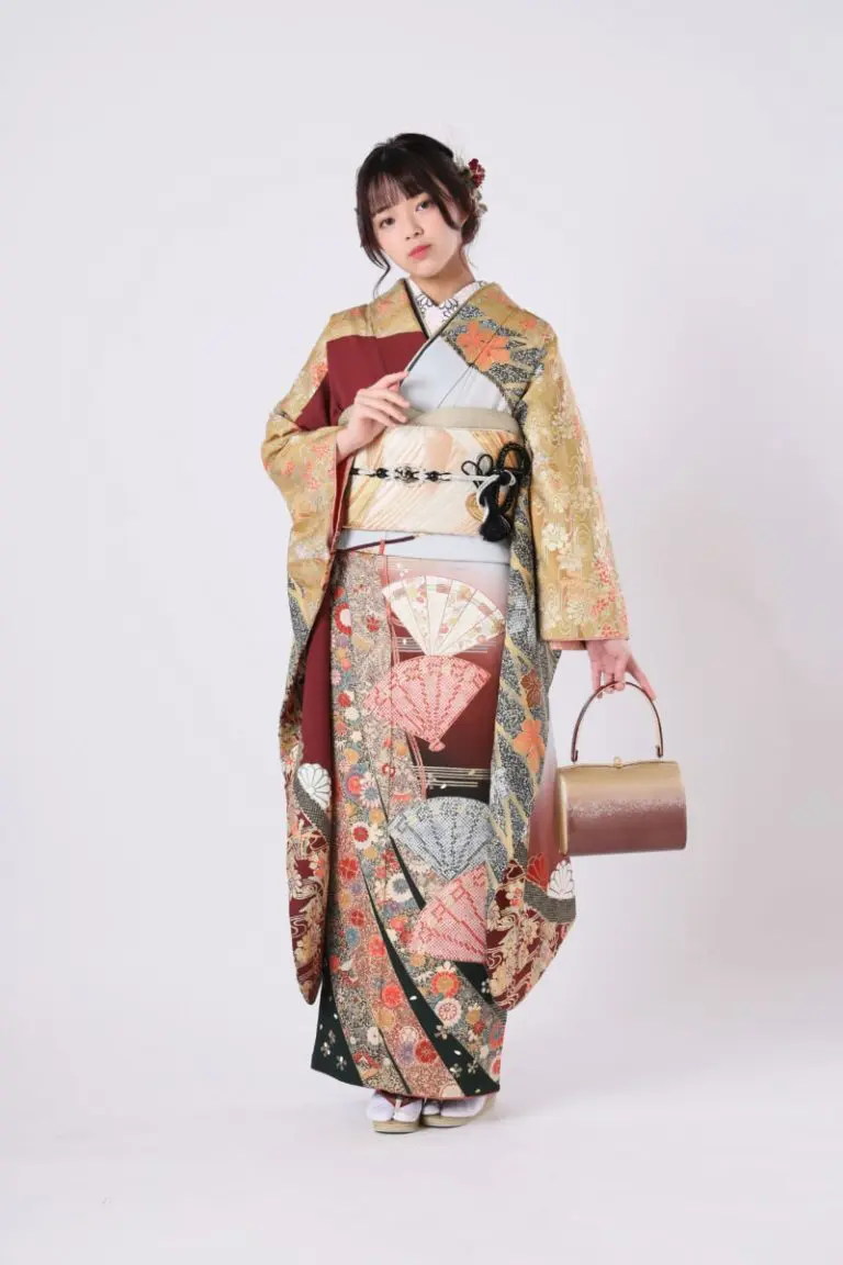 複雑な模様と花のモチーフがあしらわれた伝統的な着物を着た人物が、シンプルな背景に立っています。小さなハンドバッグを持ち、髪飾りで凝った髪型をしています。.