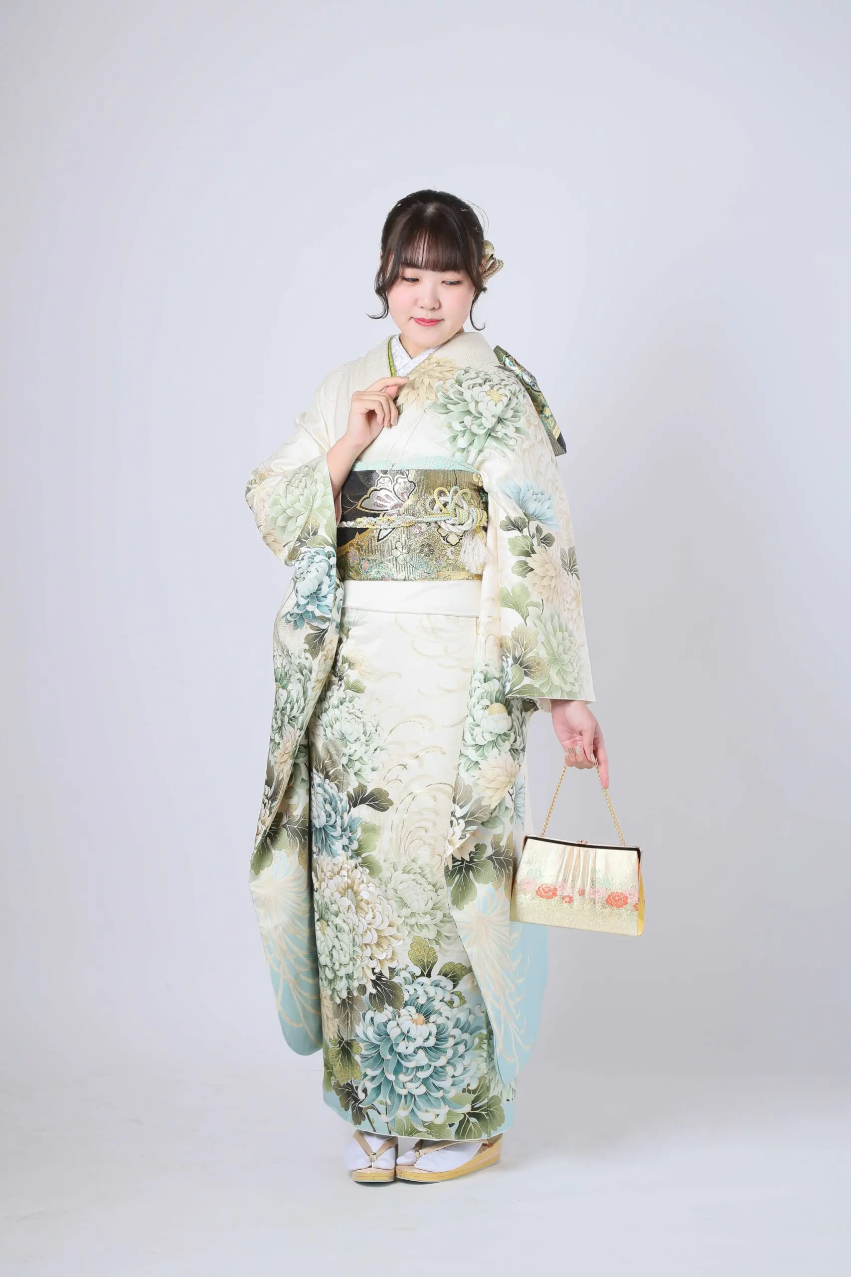 伝統的な令和7年成人式、川口市の落ち着いた花柄の着物を着た人物が、無地の背景に小さなハンドバッグを持ち、伝統的な履物を履いて立っています。.
