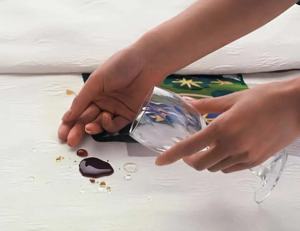 倒れたワイングラスを持った人が、白いテーブルクロスの上に赤ワインをこぼしています。近くには数滴の滴と模様のついたナプキンが見えます。.