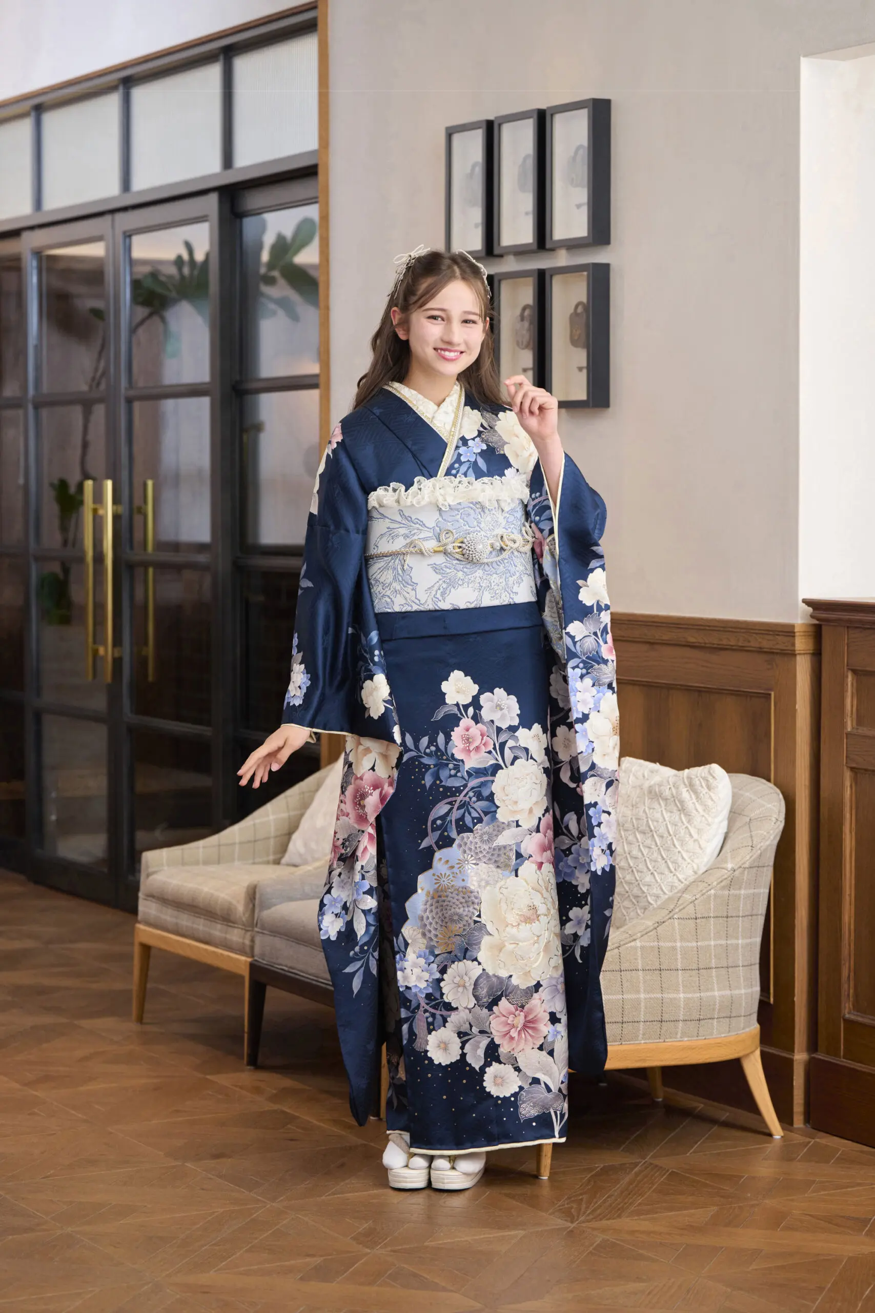 濃紺の花柄の着物に水色の帯を締めたM-412を着た女性が室内に立っている。片袖を持って微笑み、ソファと壁に飾られた額縁の前でポーズをとっている。.