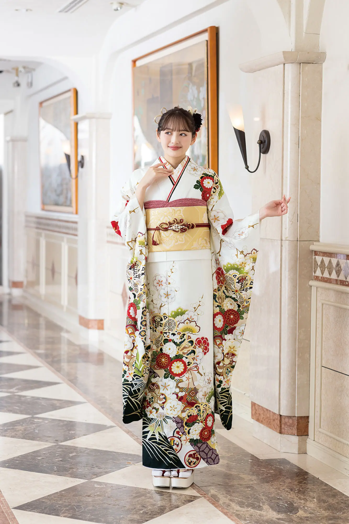 大理石の床とウォールアートが施された廊下に、K-120-色とりどりの花柄が描かれた白い着物に金の帯を締めた人物が立っている。髪には飾りをつけ、着物の袖を広げている。.