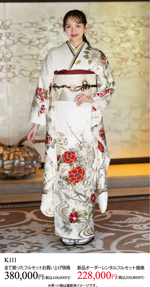 赤と金の花模様の白い着物を着て、ベージュの帯を締めた女性が室内に立っている。下のテキストには、商品コードK111とともに、日本円での購入とレンタルの2つの価格が表示されています。.