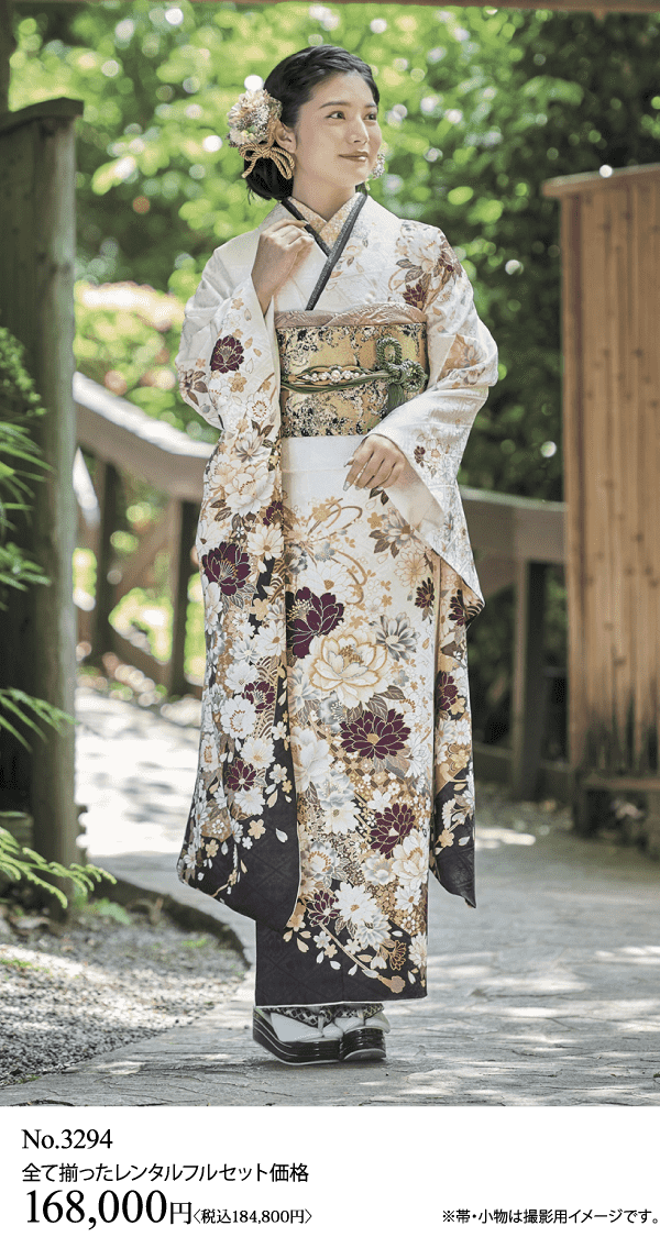 白と金の花柄の着物に緑の帯を締めた女性が、屋外の小道に立っている。凝ったヘアアクセサリーをつけ、木製の草履を履いている。価格と商品情報は画像の下に表示されています。.