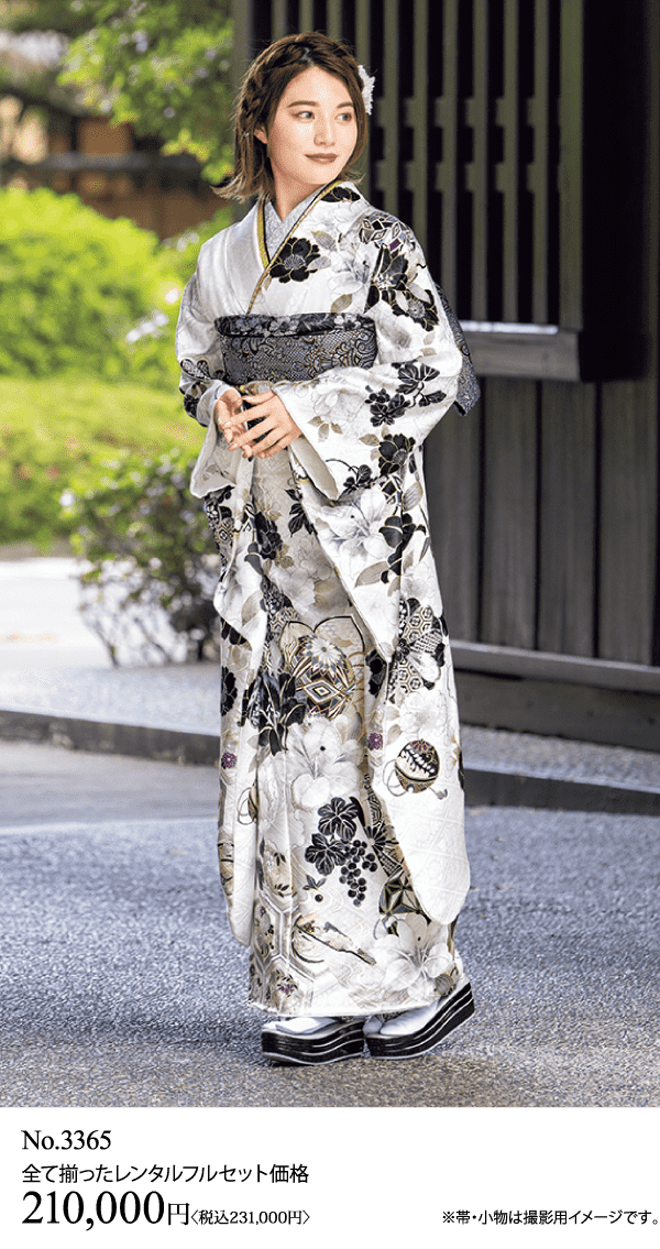 白と黒の花柄の着物に帯を合わせた女性が外に立っている。小さなクラッチバッグを持っている。下のテキストには、レンタルセットNo.3365、価格210,000円（税込231,000円）、付属品についての注意書きがある。.