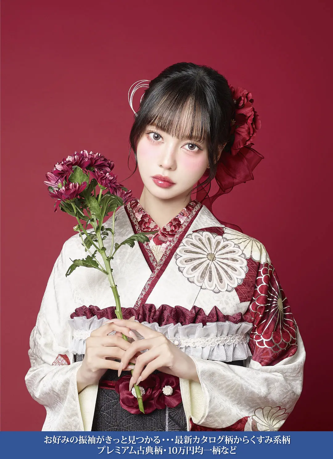 深紅の背景に、白とワインレッドの花柄の着物を着た若い女性が、濃い赤の花を持って立っている。前髪のあるストレートヘアに装飾的なヘアアクセサリー。下部に日本語のテキストが表示されている。.