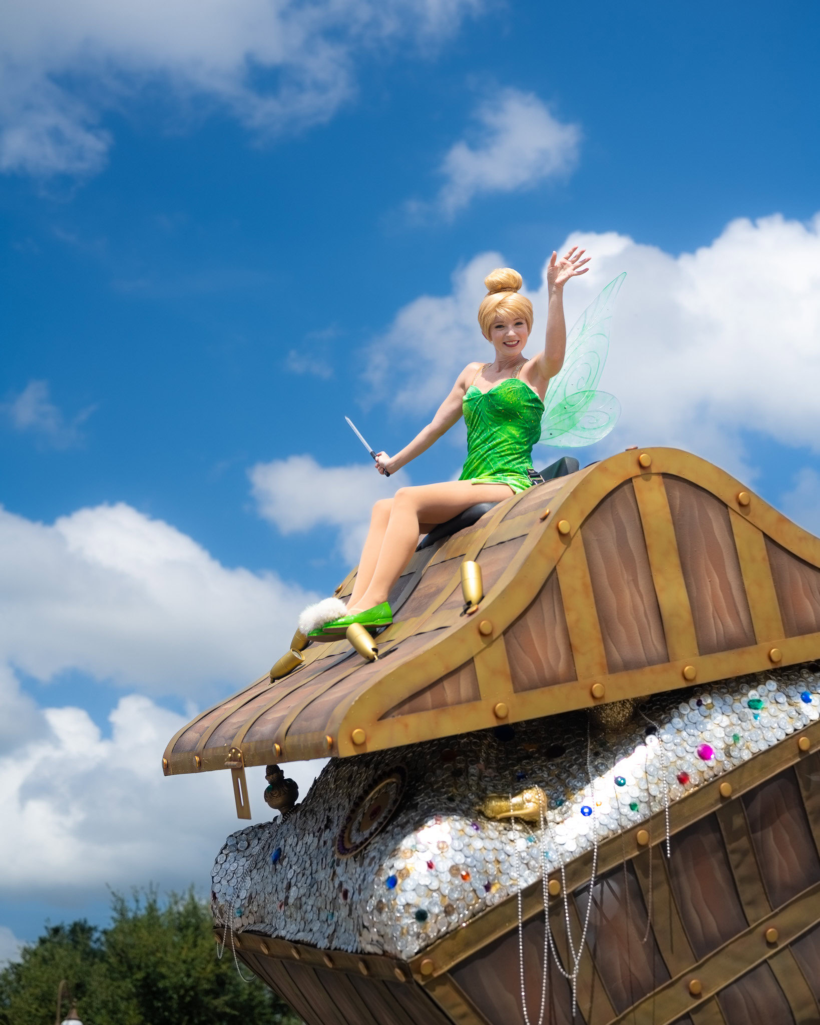 Campanilla ondeando desde una carroza de desfile en Magic Kingdom bajo un cielo azul