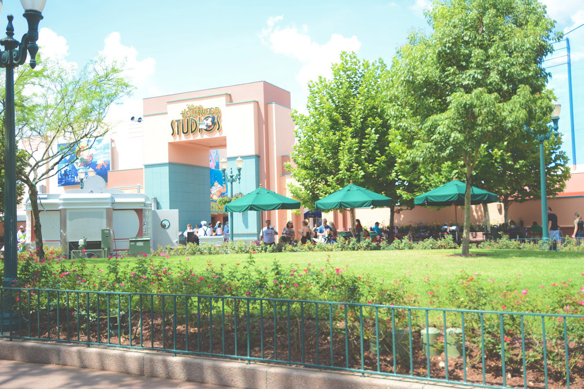 Entrada a Disney's Hollywood Studios con sombrillas verdes y zona de asientos para invitados.