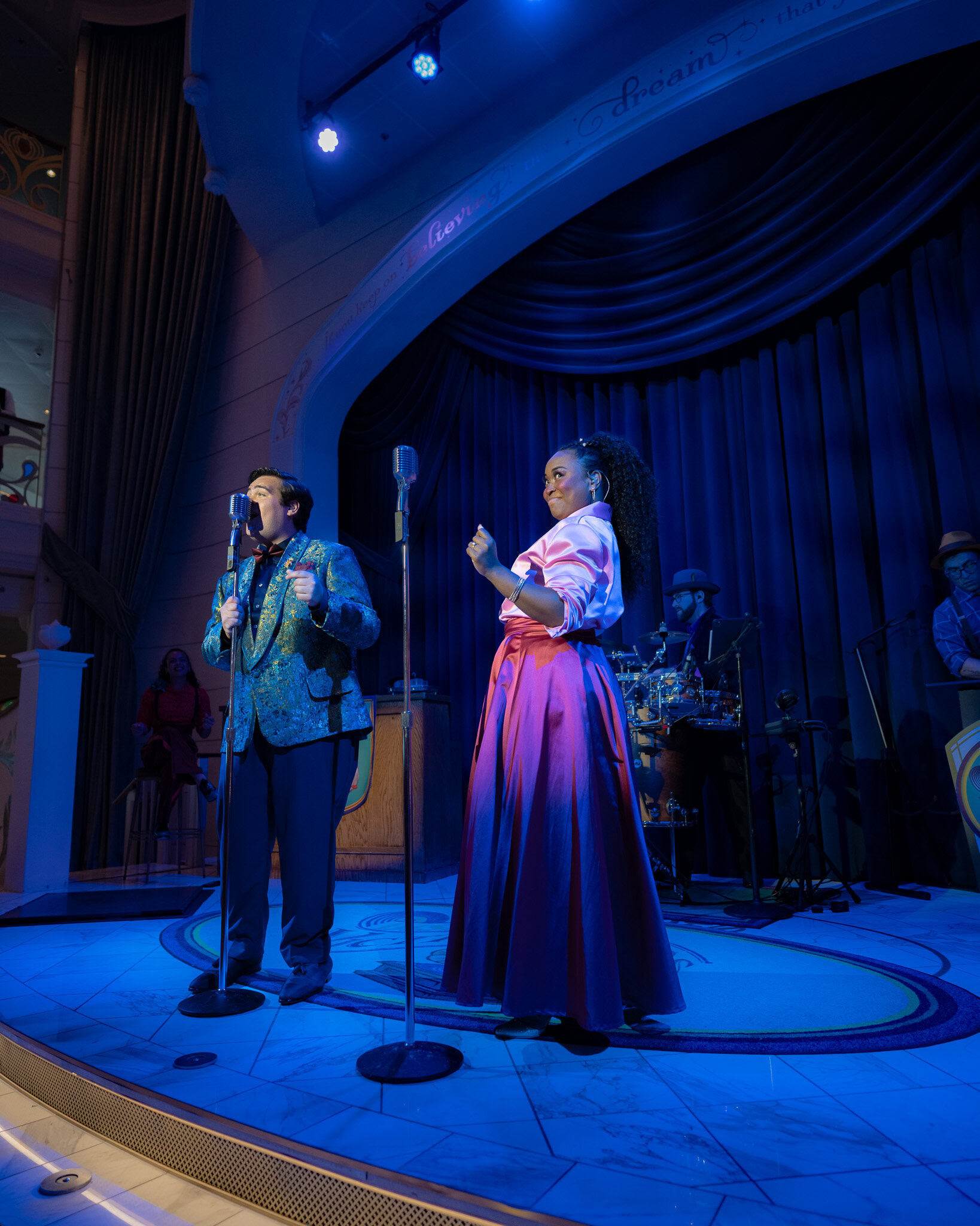 Live performers singing in the Grand Hall aboard the Disney Wish with blue stage lighting and live band