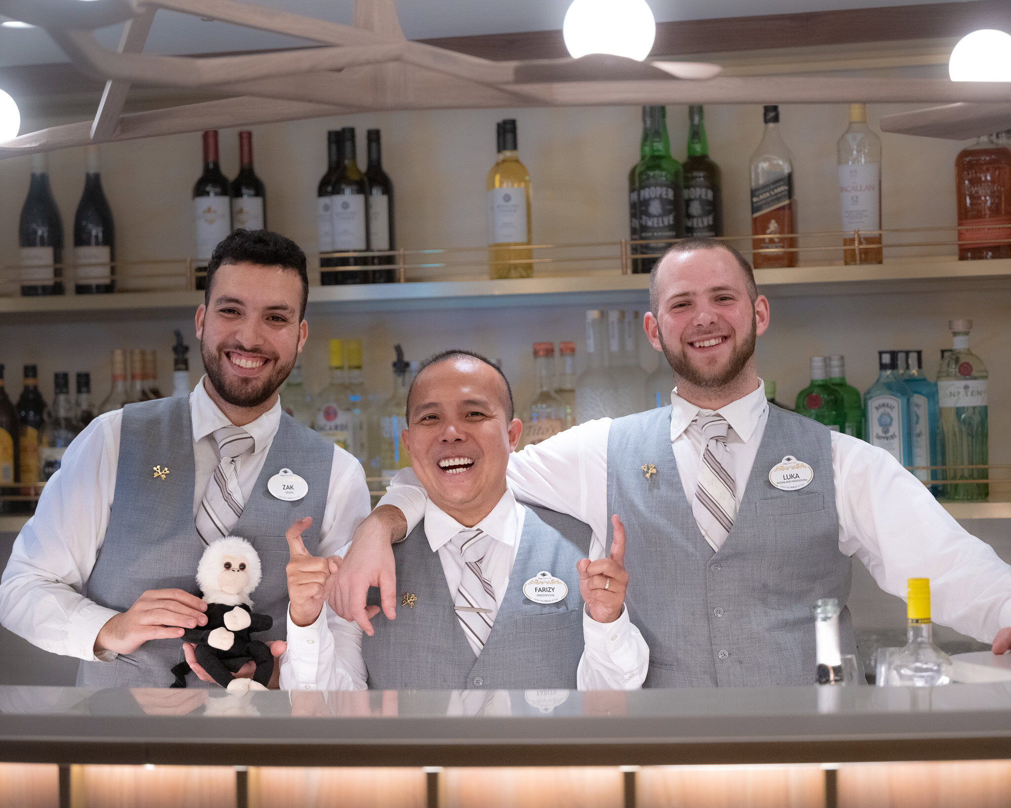 Disney Magic Concierge team members Zak, Farizy, and Luka smiling behind the bar during a Concierge sailing.