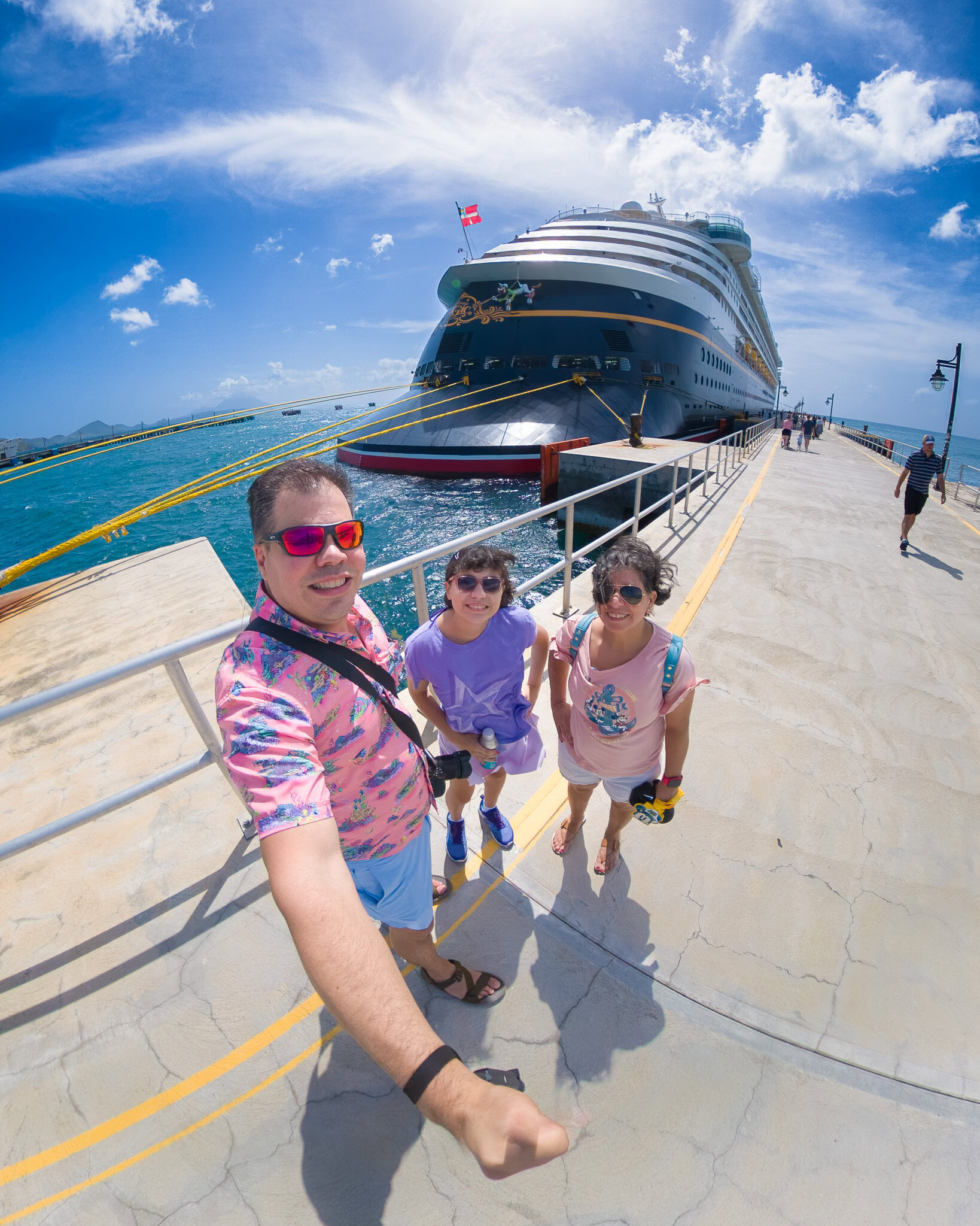 Raúl, Lucy, and Daniela standing on the pier in St. Kitts with the Disney Magic docked behind them.