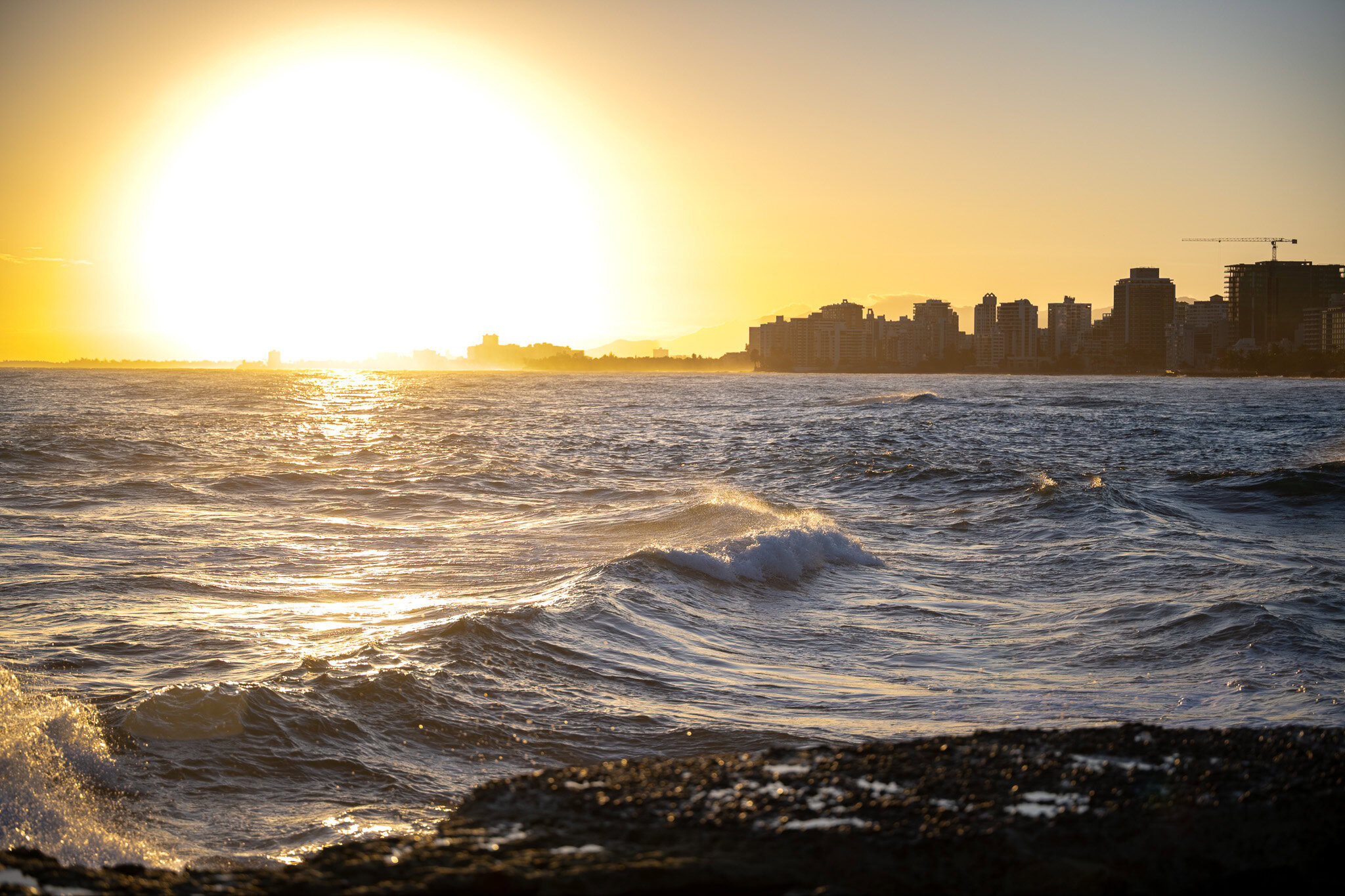 Sunset over waves at Escambrón Beach in San Juan, Puerto Rico with the city skyline in the background.