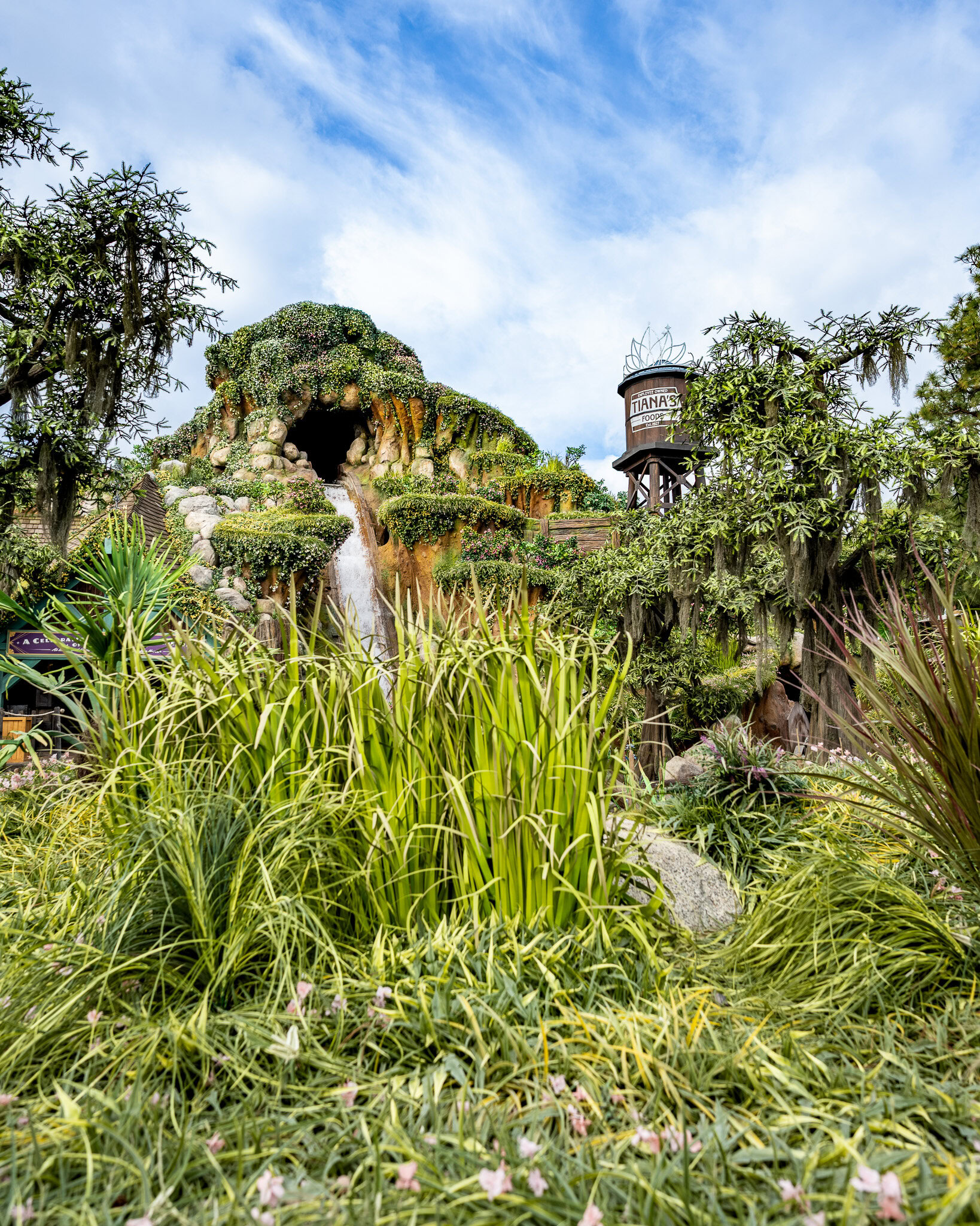 Entrance of Tiana’s Bayou Adventure with lush greenery and water feature at Disneyland.