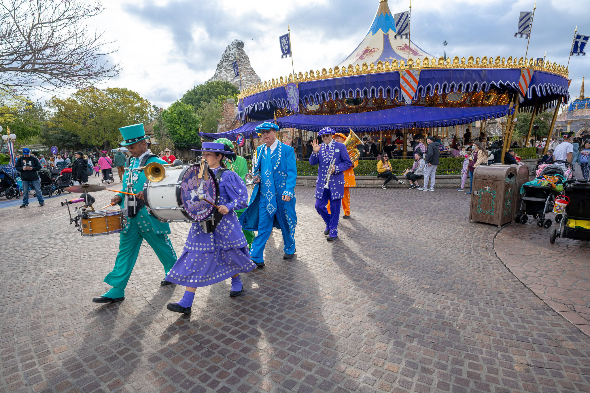 Disneyland parade performers in colorful costumes marching near King Arthur Carousel.
