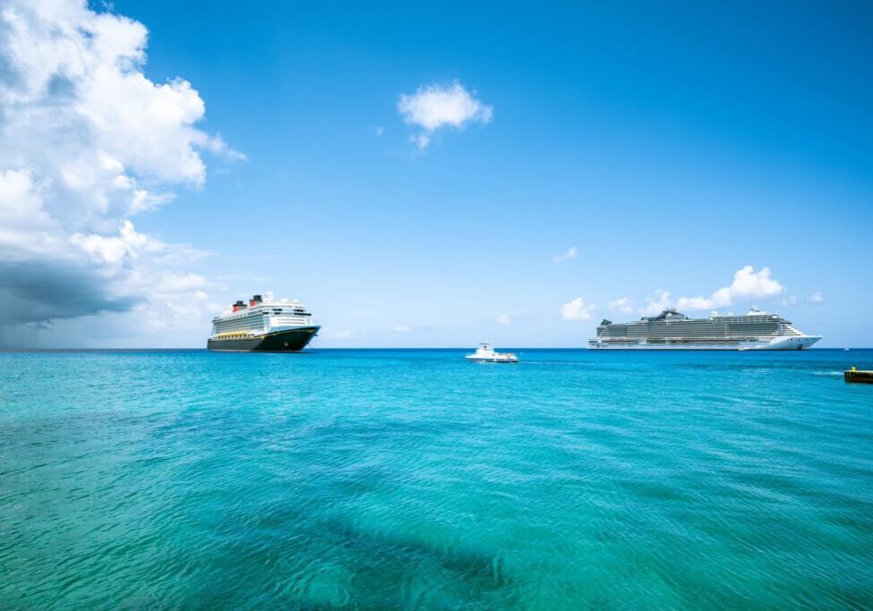 Disney Fantasy docked off the coast of Grand Cayman with clear blue waters and another cruise ship in view.