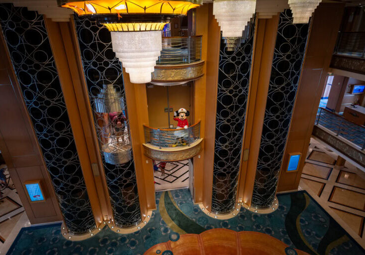 Captain Minnie Mouse waving from a decorated balcony in the Disney Magic Atrium during San Juan sailing