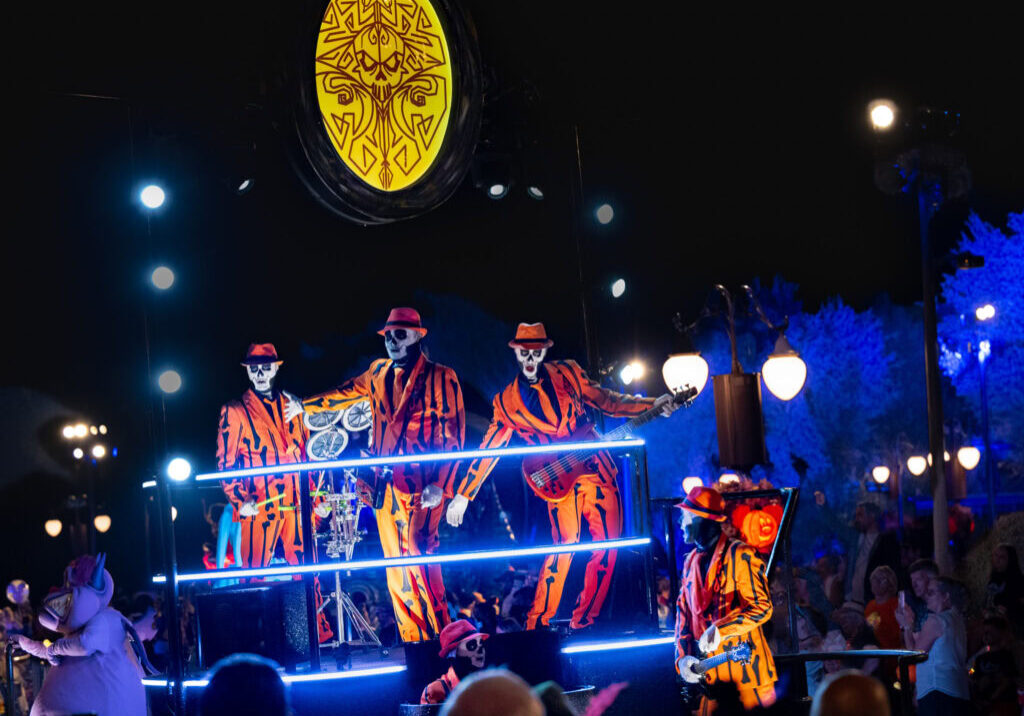 Skeleton band performers in bright orange striped suits playing instruments on a glowing float during Mickey’s Not-So-Scary Halloween Party parade at Magic Kingdom.