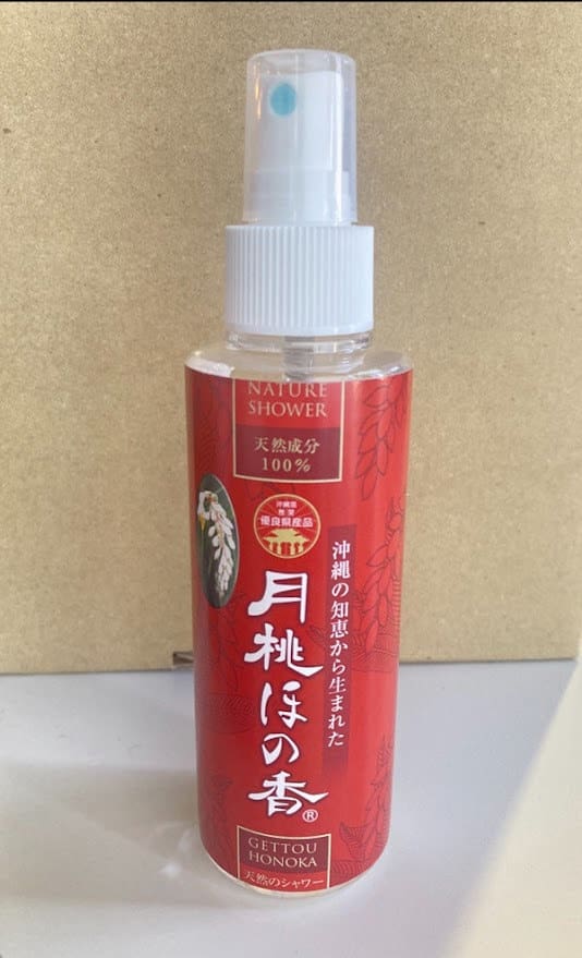 ベージュの背景に「Nature Shower」と書かれた赤いスプレーボトル。白いスプレーノズルとキャップ。.
