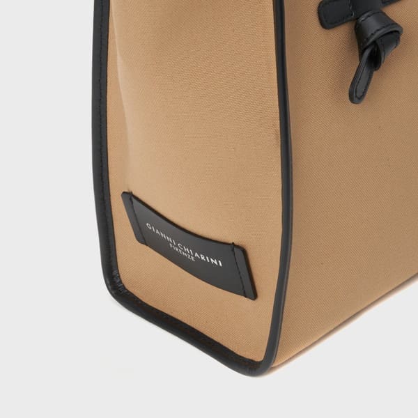 ベージュのジャンニキアリーニ製ハンドバッグのアップ。黒い縁取りと "GIANNI CHIARINI FIRENZE "の黒いラベル。角と側面の一部が見え、黒いレザーストラップのディテールもある。イタリア製の上質なデザイン。.