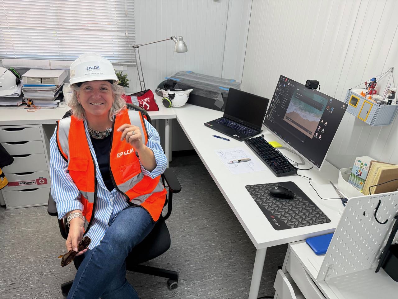 Profissional de Cuidados Paliativos Pediátricos Madrid CAPPI  Fundación porqueViven , a sorrir ao lado da sua secretária enquanto gere a licença de cuidados paliativos pediátricos em Madrid. CAPPI  Fundación porqueViven 